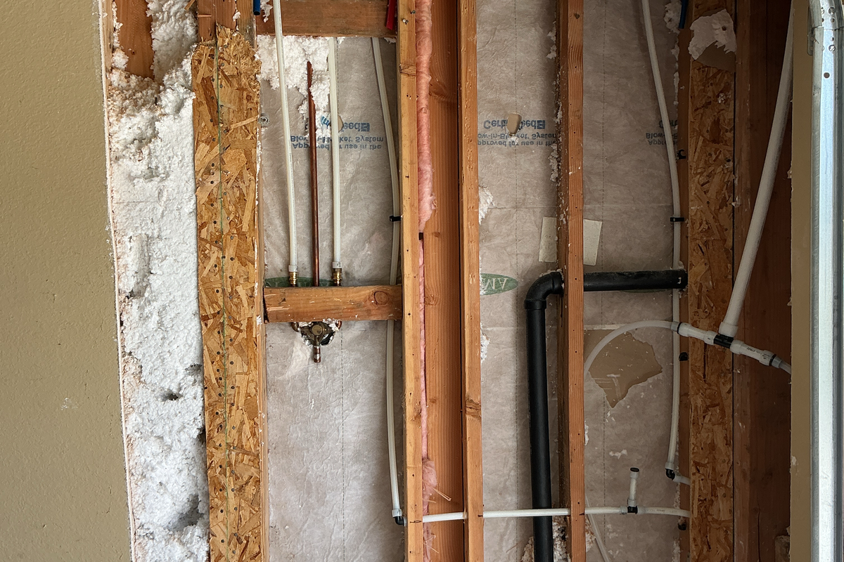 New PEX supply lines run through opened stud bays and strapped, with copper stub-outs and shutoff valves at a branch
